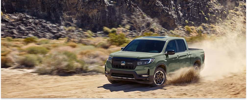 Front three-quarter view of a green 2026 Honda Ridgeline pickup truck driving on a dusty off-road trail.