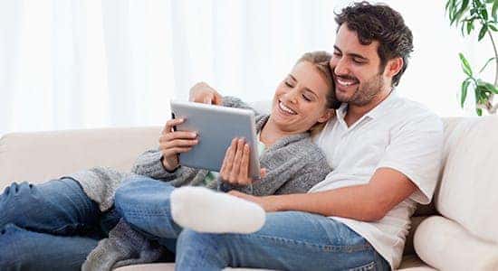 Happy couple on couch online shopping on a tablet
