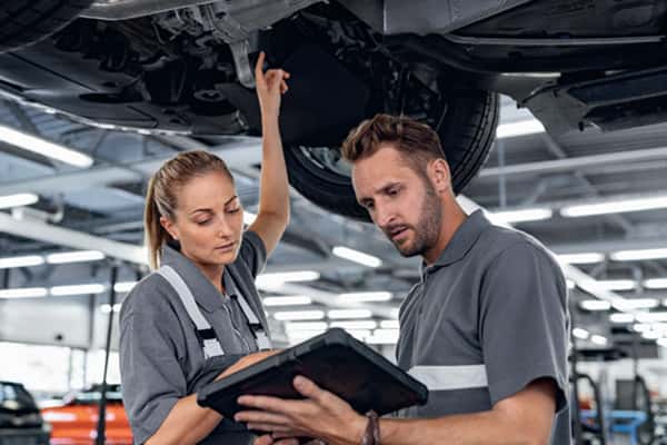 Service advisor and technician reviewing a digital vehicle inspection tablet under a lifted BMW