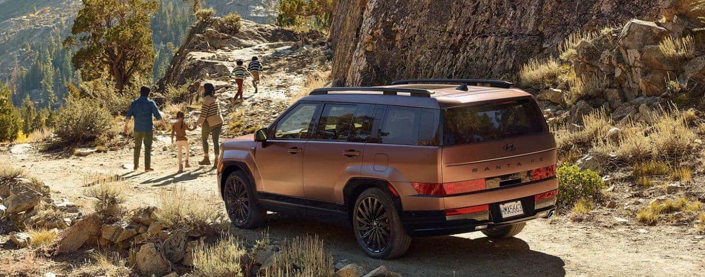 Brown 2026 Hyundai Santa Fe rear view while parked on a trail with a family leaving.