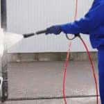 Worker cleaning automobile floor mats with high pressure water