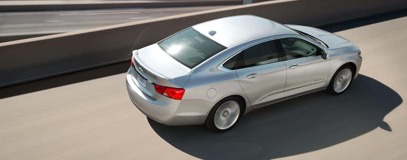 A silver 2020 Chevy Impala is driving on a highway overpass.