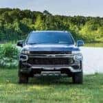 A gray 2021 Chevy Suburban is shown from the front parked in front of a lake.