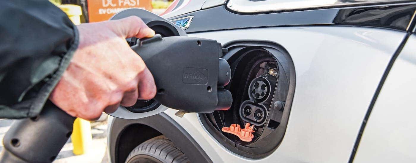 A closeup shows the charging port on a silver Chevy EV, a 2021 Chevy Bolt EV.