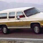 A tan two-tone 1991 used Chevy Suburban is towing a camper on a mountain road.