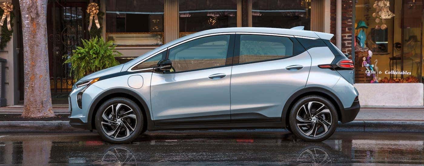 A silver/blue 2022 Chevy Bolt EV is shown from the side parked in front of a row of stores.