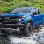 A blue 2022 Chevy Silverado 1500 ZR2 is shown off-roading through a river.