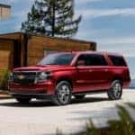 A red 2020 Chevy Suburban is shown from the front parked in front of a modern house after leaving a Lexington used car dealer.