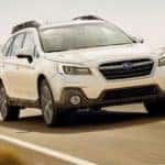 A white 2019 Subaru Outback is shown from the front driving on an open road.