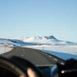 person riding vehicle on paved road between snow field