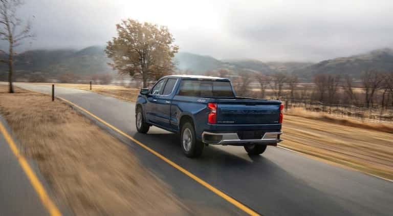 A blue 2020 Chevy Silverado 1500 is shown from a rear angle driving on a road.