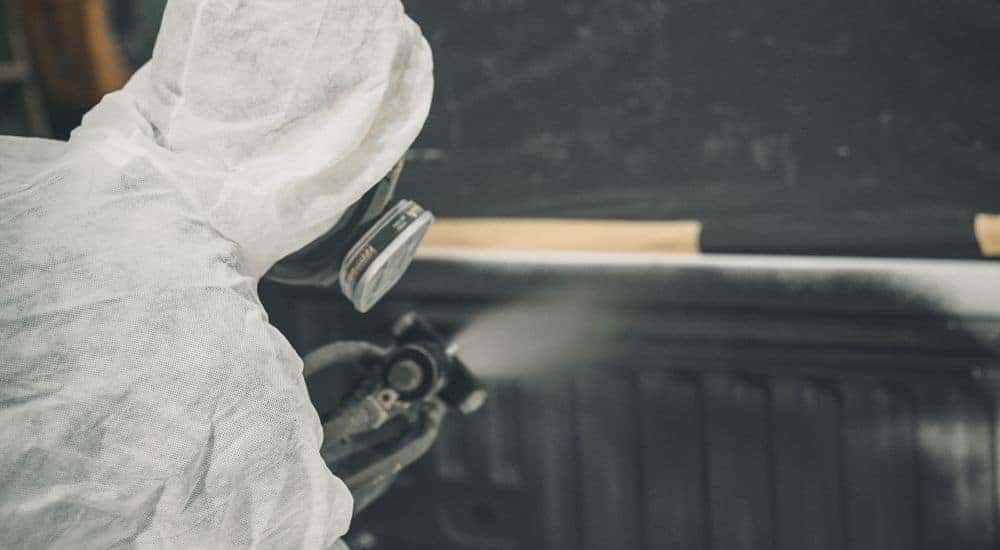 A person is shown applying spray-on bed liner.