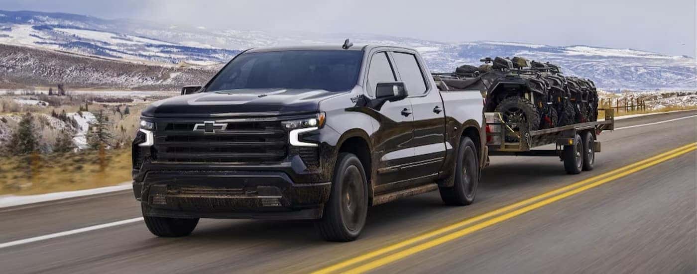 A black 2024 Chevy Silverado 1500 High Country is shown towing a trailer.