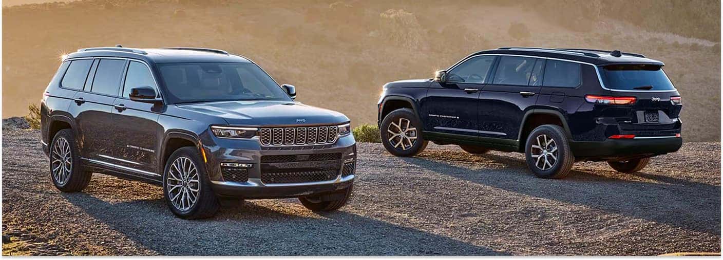 Two 2026 Jeep Grand Cherokee SUVs parked on a dirt trail at sunset.