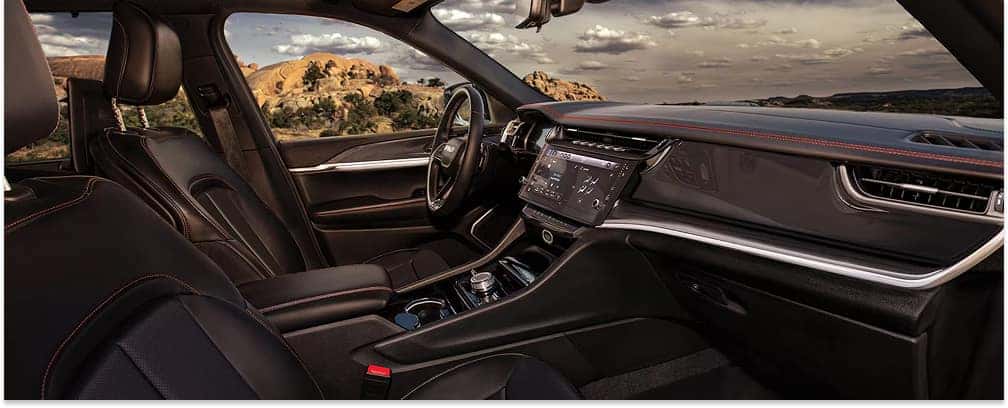 Black leather interior cabin of a 2026 Jeep Grand Cherokee with red accent stitching and digital displays.
