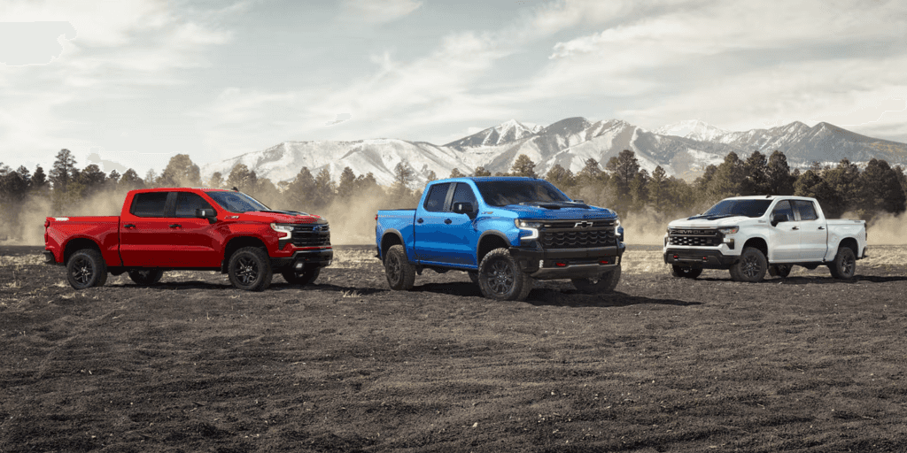 Three 2026 Chevrolet Silverado 1500 models parked against a mountainscape