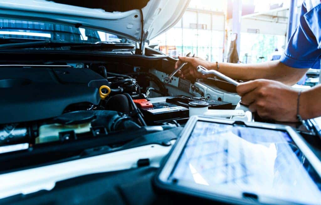 hands working inside a car hood, inspecting engine