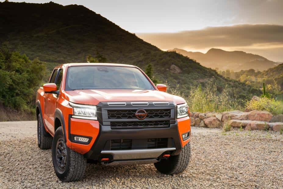 2025 Nissan Frontier in Afterburn Orange parked outside Kelly Nissan dealership, showcasing bold new grille, LED headlights, and rugged stance.
