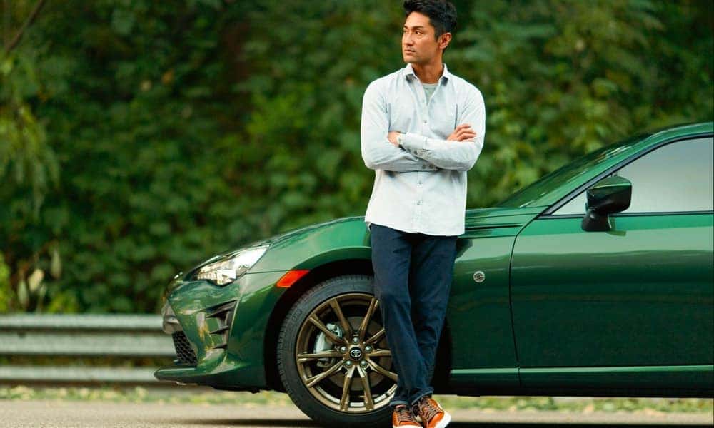 Man leaning against green car parked on the side of the road