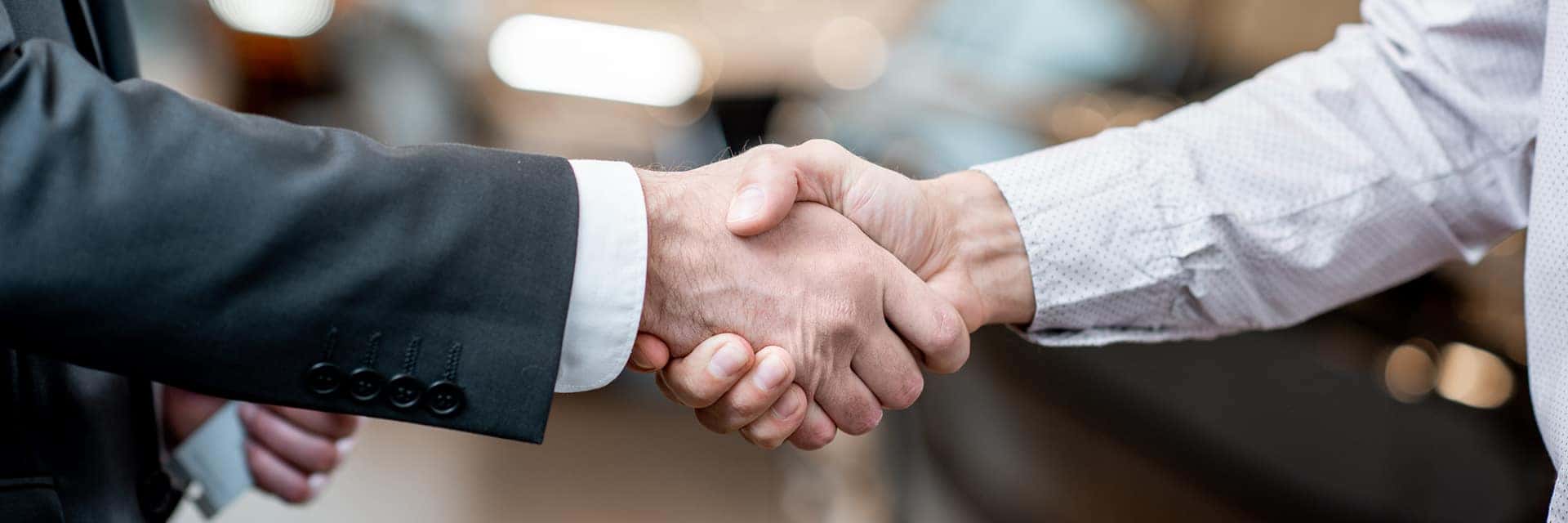 two people hand shaking in front of a car at a dealership