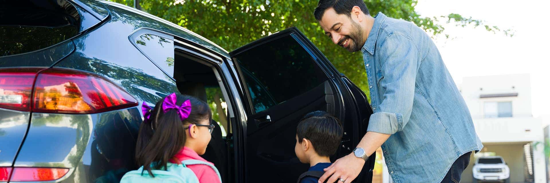 father helping kids with backpacks into car