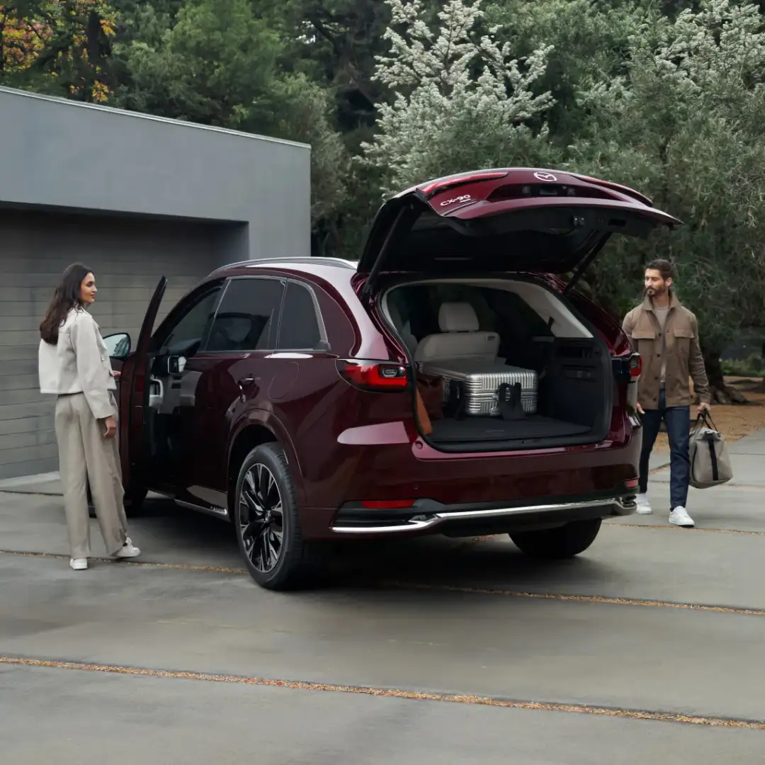 A family loading cargo into a Mazda CX-90 in a driveway
