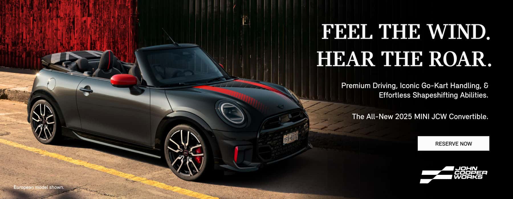 Black and red MINI JCW convertible parked on a city street in front of a black and red wall.