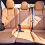 Interior view of a vehicle's rear bench featuring three tan leather seats with perforated detailing and black seatbelts.