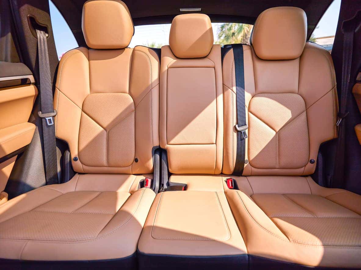 Interior view of a vehicle's rear bench featuring three tan leather seats with perforated detailing and black seatbelts.