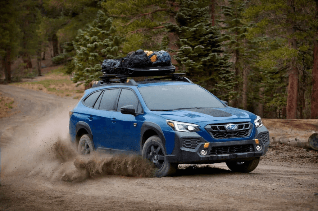A blue Subaru Outback with bags on top drifting in a forested off-road