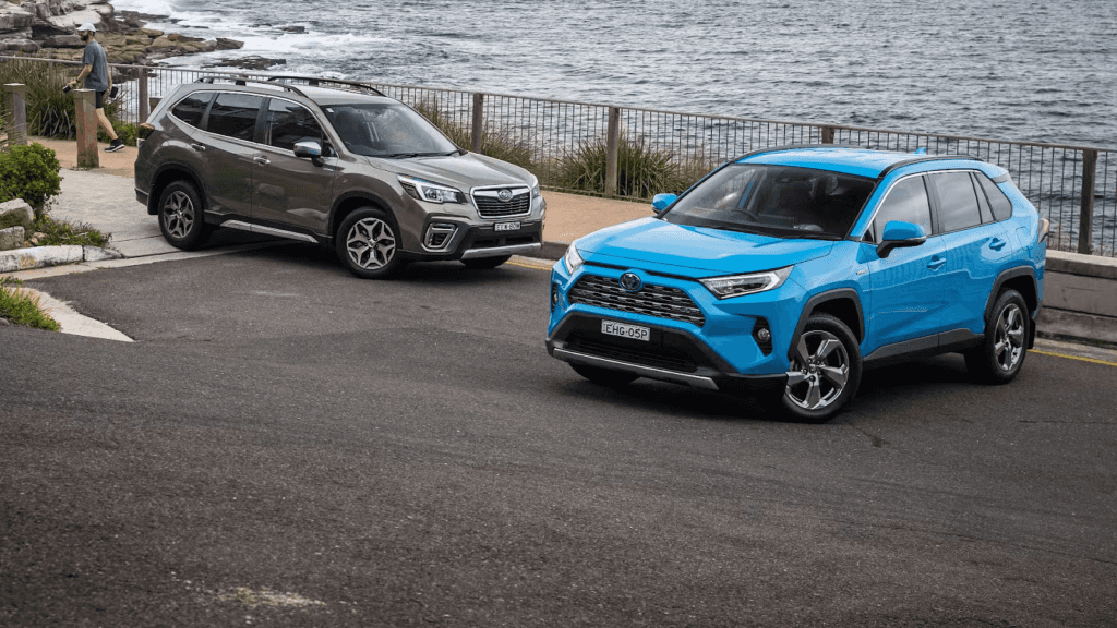 2025 Subaru Forester and 2025 Toyota RAV4 Hybrid parked by the ocean on a coastal road, showcasing exterior design and color options.