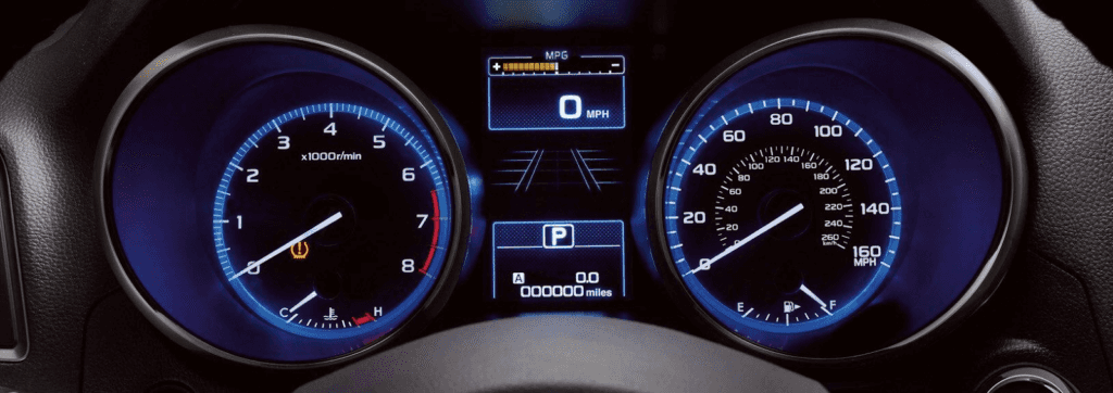 A close-up view of a vehicle's instrument cluster displaying the analog tachometer and speedometer with blue backlighting. The central digital screen shows the odometer at 0.0 miles, 0 MPH, the gear in Park (P), and a tire pressure warning light illuminated on the tachometer.