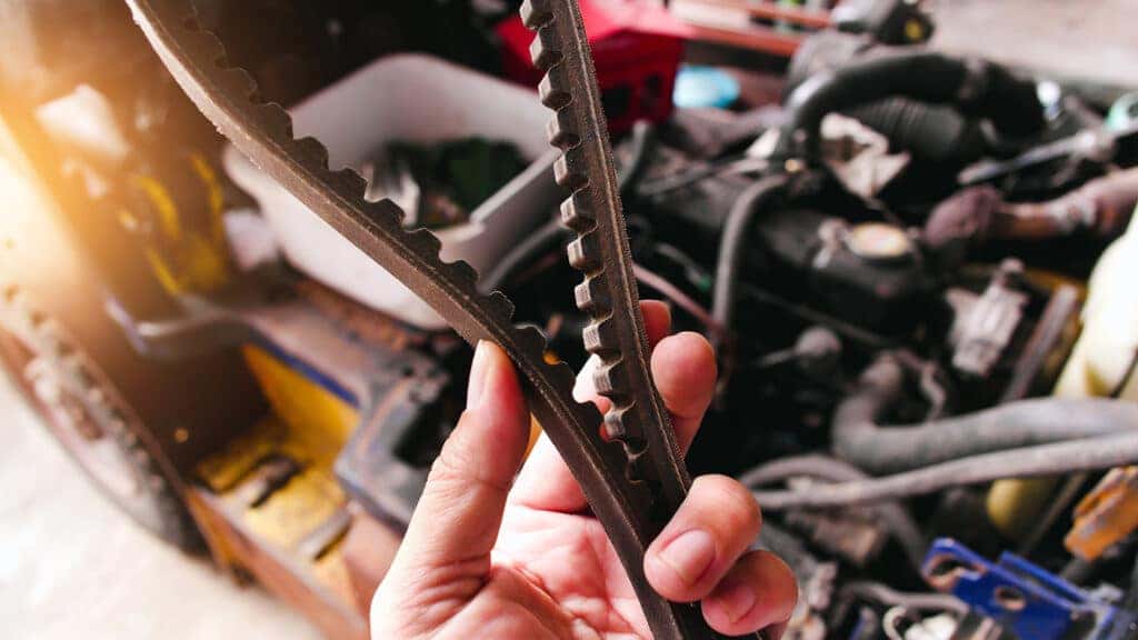 A technician holding a vehicle's timing belt
